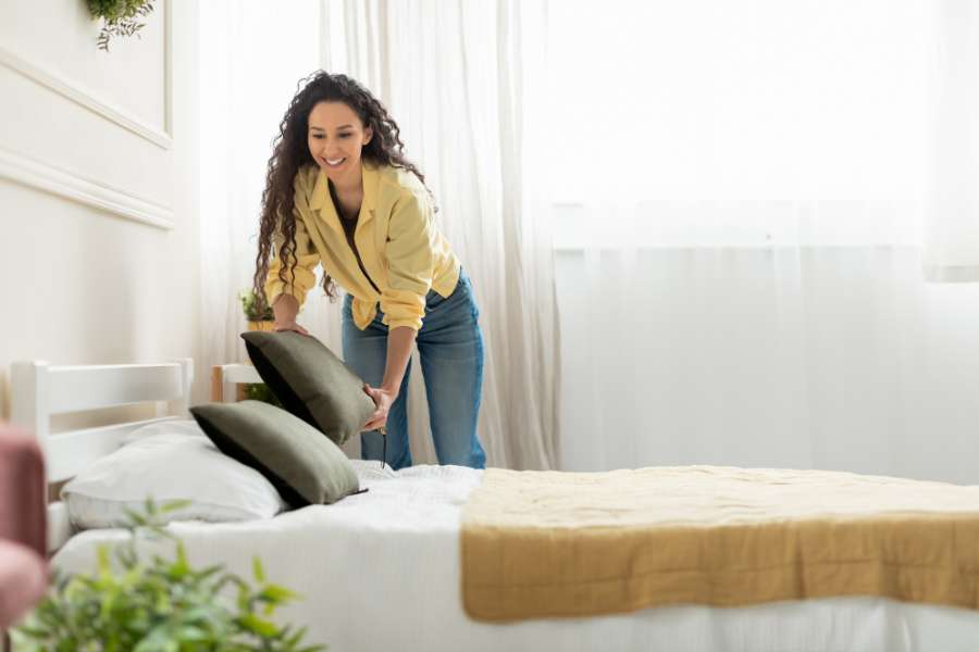 woman making bed while smiling