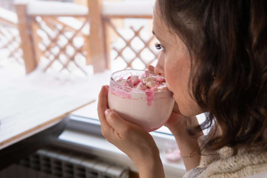 woman sipping a pink drink with marshmallows in a tranparent mug