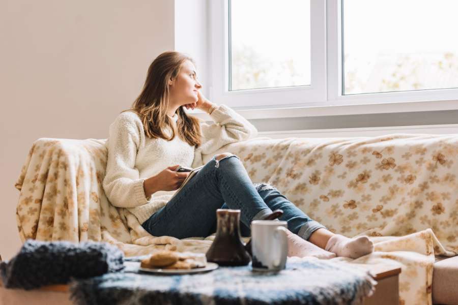 woman on couch looking out the window, holding phone