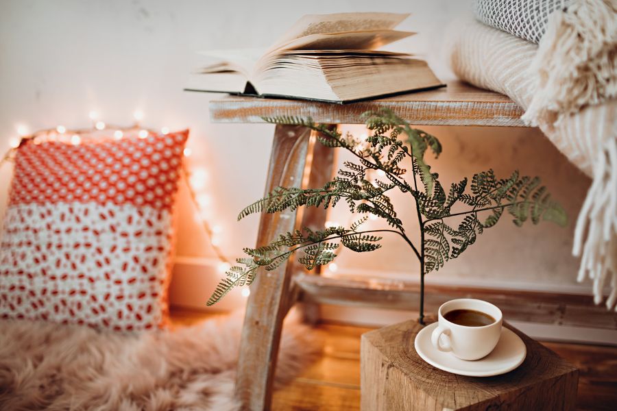aesthetic view of book on table, fairlights, cushion, and coffee in cup and saucer on wooden table