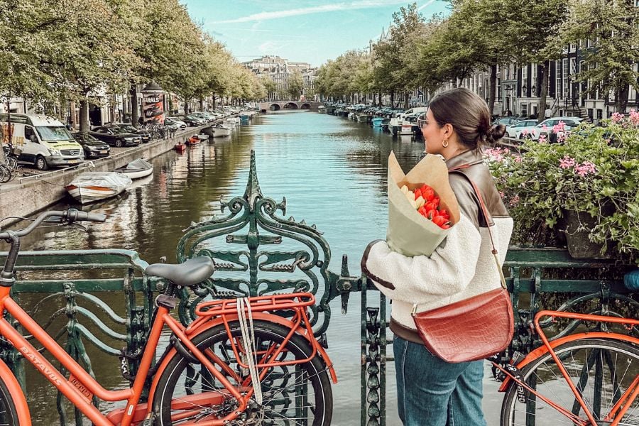 womam holding bouquet standing by bicycles facing a canal in Amsterdam