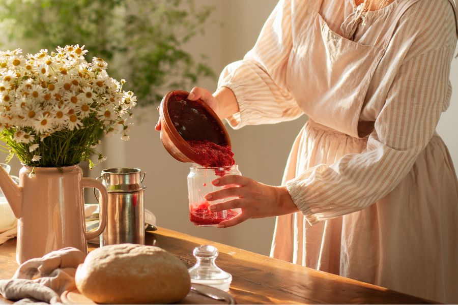 hand pouring red puree into a jar
