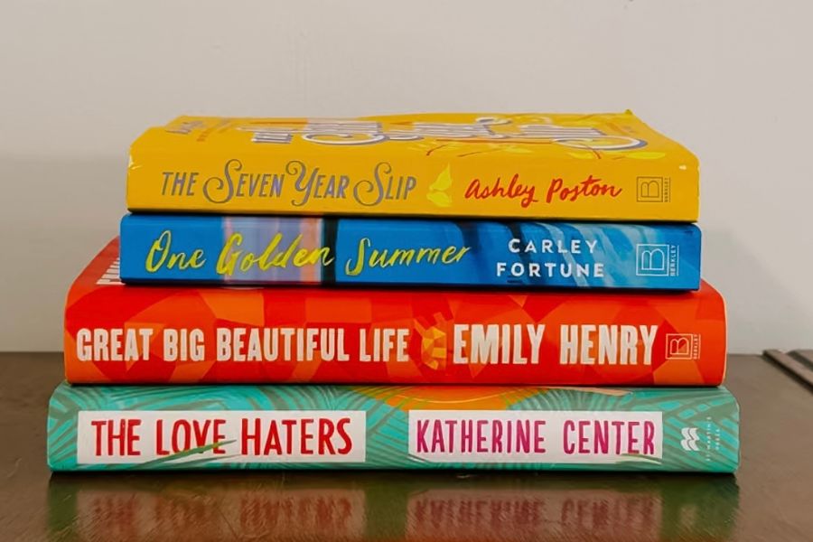 Four books on top of each other on table: The Seven Year Slip, One Golden Summer, Great Big Beautiful Life, and The Love Haters