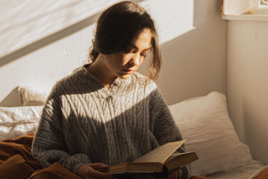 woman in grey knit sweater reading in bed