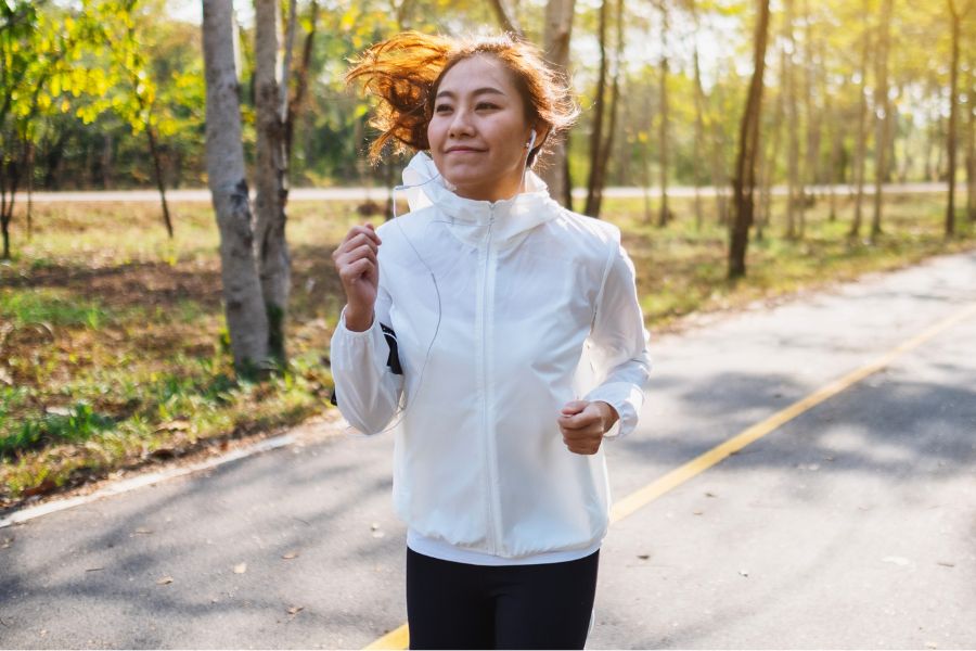 woman running with wired earphones plugged in, wearing white sports jacket